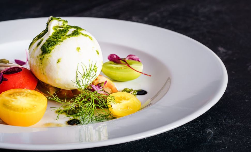 mozzarella on a plate with sliced fruits, vegetables, and herbs