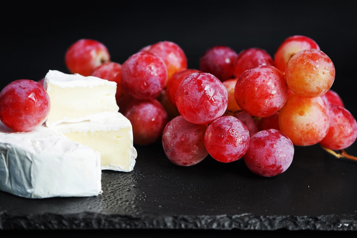 brush of large pink grapes next to brie cheese