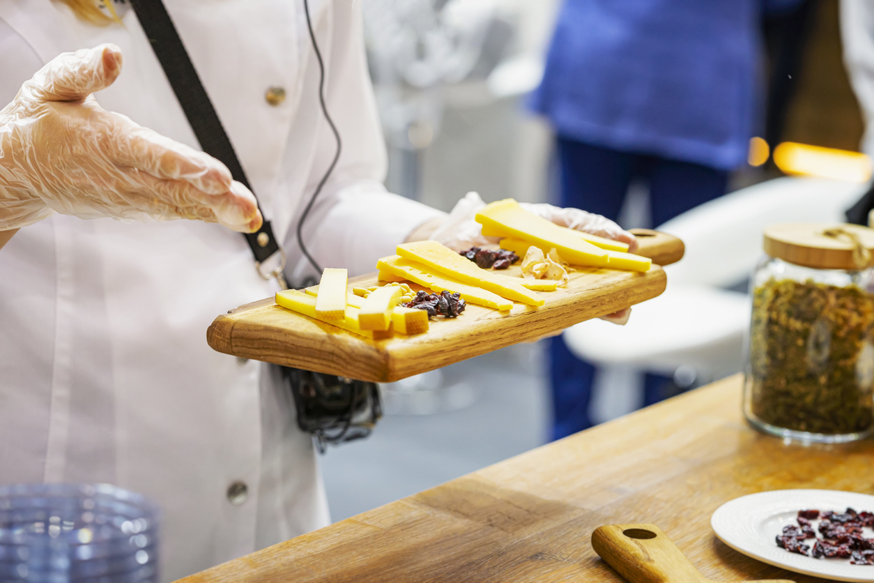 a chef inviting customers to try the cheeses on her cheese board