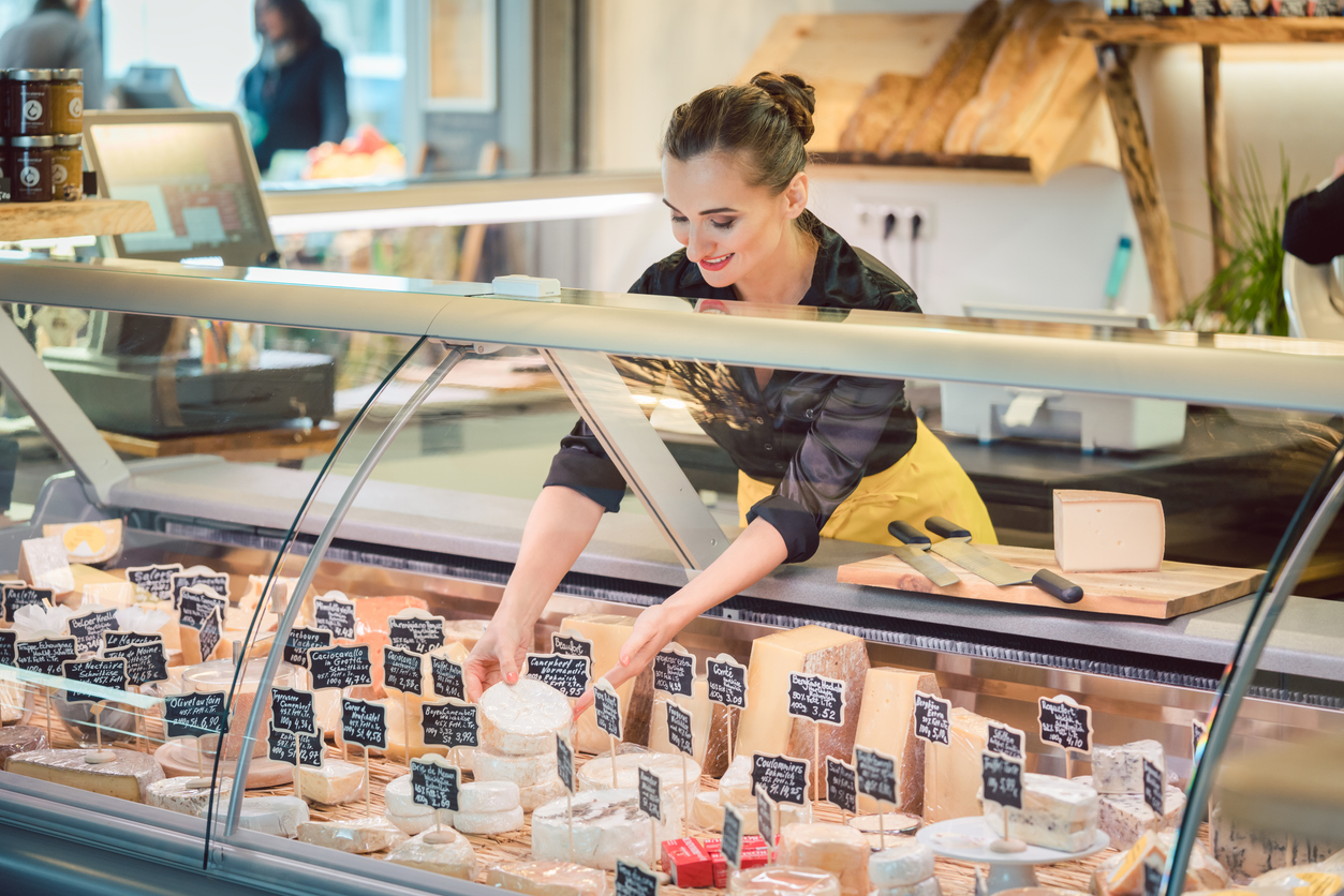 Shop clerk woman sorting cheese in the store display to sell it