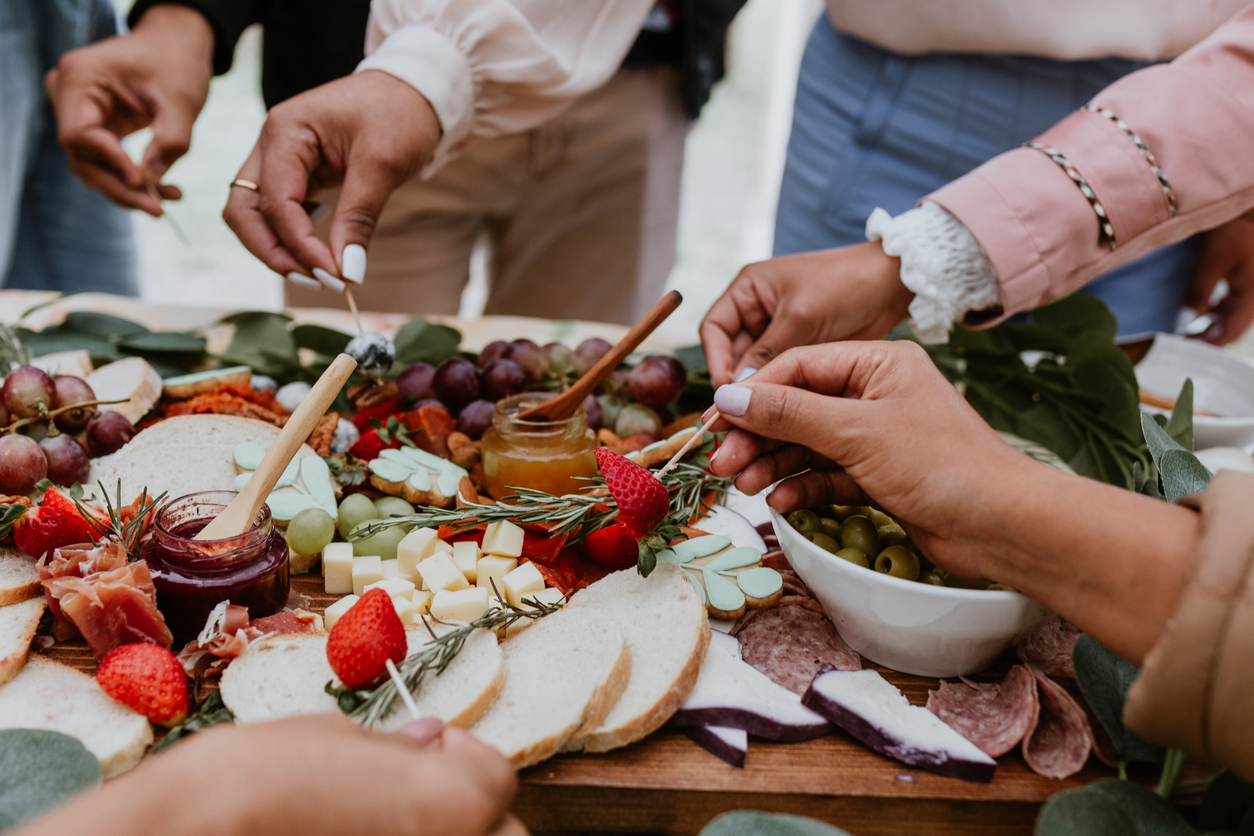 hands and Outdoor charcuterie board with wine and cheese on wood table