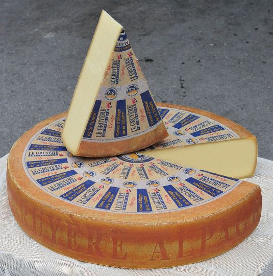 a gruyère cheese wheel with a slice on top