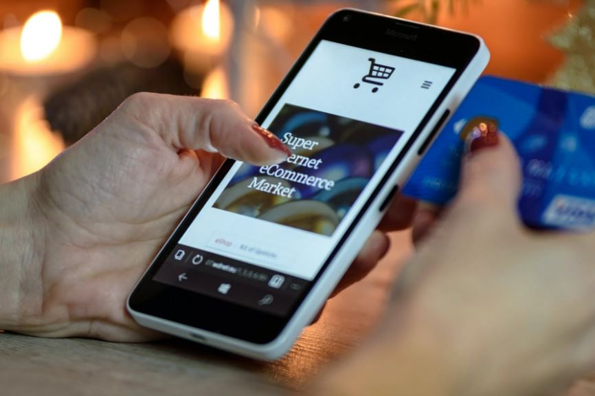 a person using a black and white smartphone to shop online and holding a blue card
