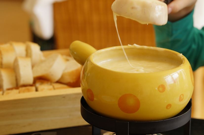 a piece of bread dipped in a bowl of cheese fondue