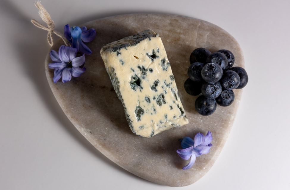 blue mold cheese, blueberries, and flowers on a wooden board