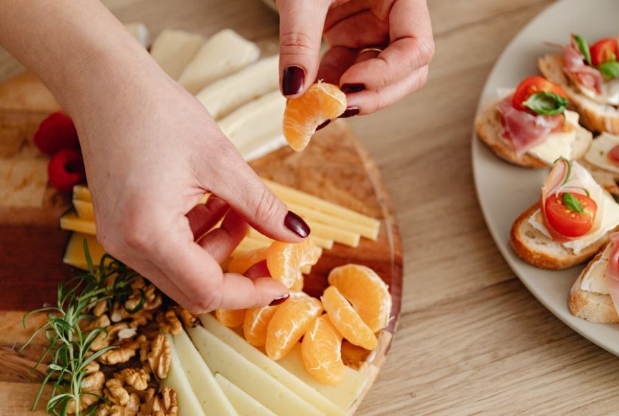 close-up photo of a person's hands placing oranges on a cheese board